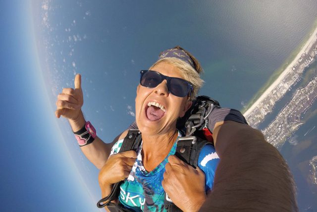 tandem skydivers freefall over beach as student smiles big